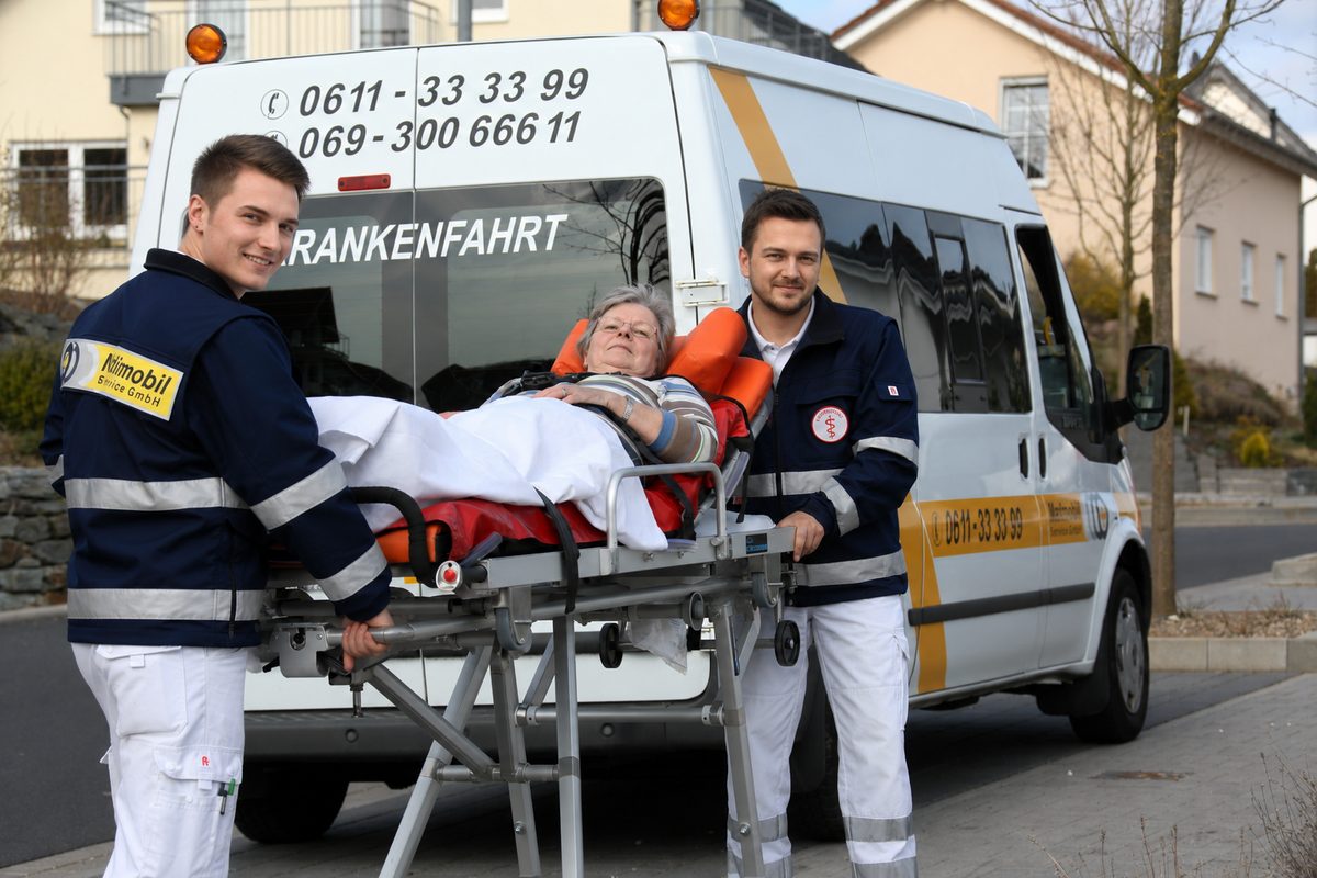 Krankenfahrtrage mit Patientin am Heck eines Medimobil-Krankenfahrzeugs